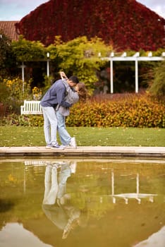 A couple in love hugs on the shore of a city pond in the European town. love story against the backdrop of autumn nature. romantic ambiance, couple goals, outdoor romance, seasonal charm, love in the city, autumnal vibes, European town, city pond, affectionate bonding, love story