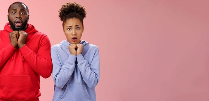 Lifestyle. Upset worried two siblings watching together scary disturbing horror movie gasping frowning cringing shock intense emotions press hands chest widen eyes terrified standing nervous pink background.