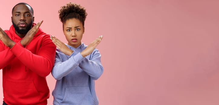 Nervous displeased two african-american man woman asking friend tell they absent not here show cross signs frowning disturbed worried begging not tell quit, stop standing pink background.