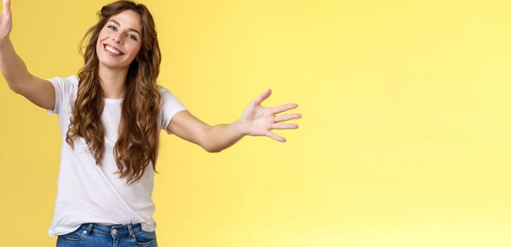 Wanna hold you tight. Romantic sincere gentle cute caucasian girl long beautiful curly hair tilt head lovely extend arms give cuddles wanna hug friend embracing dear guests yellow background.