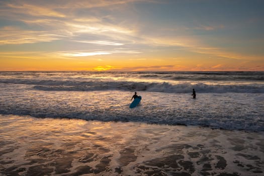 Surfer amateurs ride a board in the ocean at sunset. Aerial view