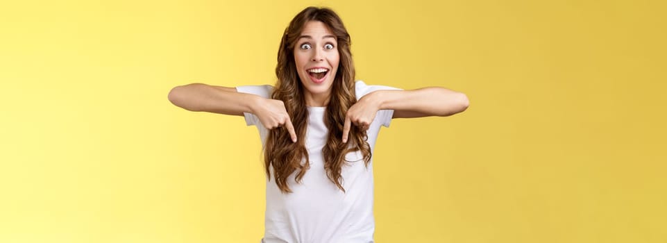 Tempting astonished impressed excited lively girl fan react stunned lose speech fascinated pointing down thrilled stare camera admiration surprise full disbelief stand yellow background.