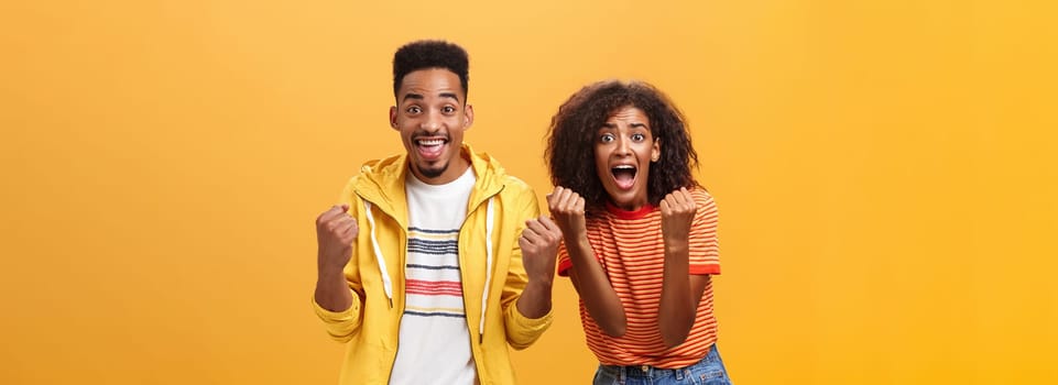 Two friends cheering and supporting mate on competition yelling joyfully clenching fists in supportive geture smiling broadly waiting with amazement and excitement for win and victory. Lifestyle.