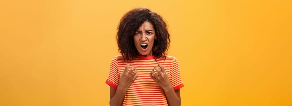 Waist-up shot of woman feeling upset feeling unfair things happened complaining and whining with regret frowning gesturing with palms near breast standing over orange background. Copy space