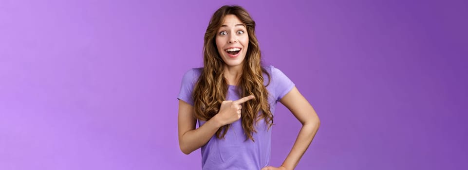 Lively excited enthuasitic good-looking woman curly hairstyle open mouth fascinated look admiration joy share awesome place location pointing left smiling broaldy thrilled purple background.