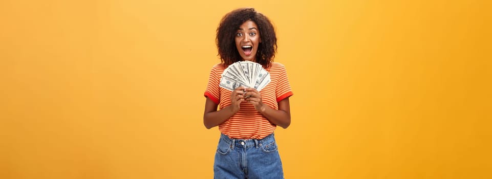 Woman cannot hide happiness winning lottery. Portrait of surprised and happy lucky african american young woman with curly hair holding bunch of money and yelling from delight receiving paycheck. Copy space