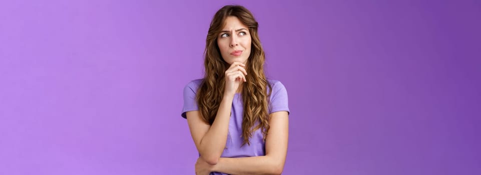 Girl trying solve problem thinking solution make hmm face smirk frowning thoughtful look away touch chin pondering making choice deciding how act what do stand purple background focused. Lifestyle.