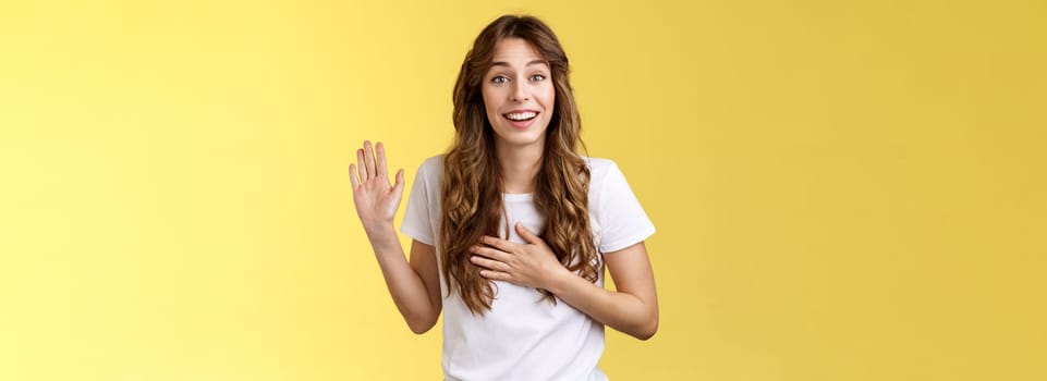 Girl introduce herself friendly joyful casual conversation smiling broadly hold hand heart raise palm waving swear tell truth be honest grinning make promise oath stand yellow background say hi. Lifestyle.