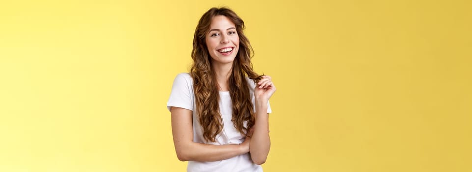 Lively joyful happy cute brunette curly long hairstyle playing curl laughing joyfully having funny amusing conversation smiling toothy white perfect smile stand yellow background relaxed.