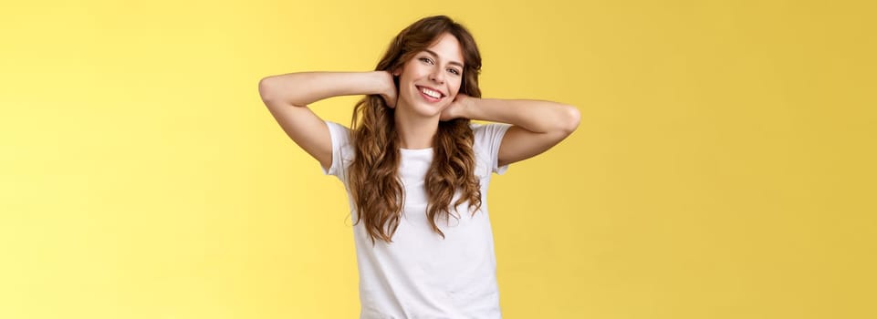 Carefree casual urban girl having summer holiday enjoy sunny perfect warm days wear white t-shirt jeans hold hands neck lazy stretch smiling broadly relaxing resting vacation stand yellow background. Lifestyle.