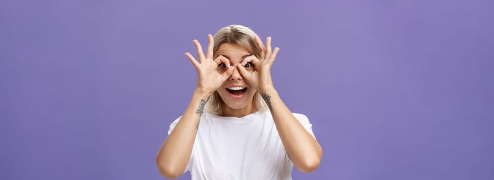 Looking at awesome discounts. Portrait of impressed amused and happy good-looking stylish young woman with tattoos on arms making circles with hands over eyes smiling with admiration at camera. Body language and advertising concept