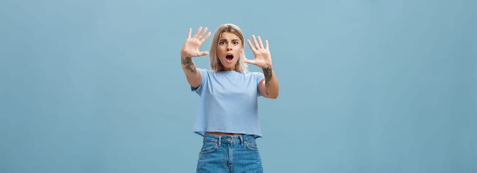 Woman terrified screaming and asking stop. Portrait of shocked panicking troubled blonde female in denim shorts and casual t-shirt pulling hands in no gesture dropping jaw and frowning. Copy space