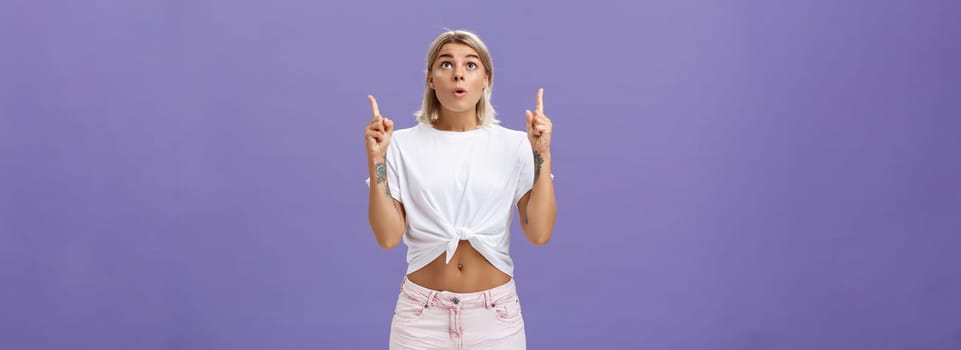 Girl dreaming become flight attendant being amazed with cool airplane flying in sky looking up with surprised impressed look saying wow pointing upwards posing over purple background. Copy space