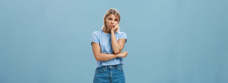 Lifestyle. Studio shot of displeased moody girlfriend feeling disappointed boyfriend spoilt date leaning head on palm sulking from dissatisfaction and squinting being offended posing over blue background.