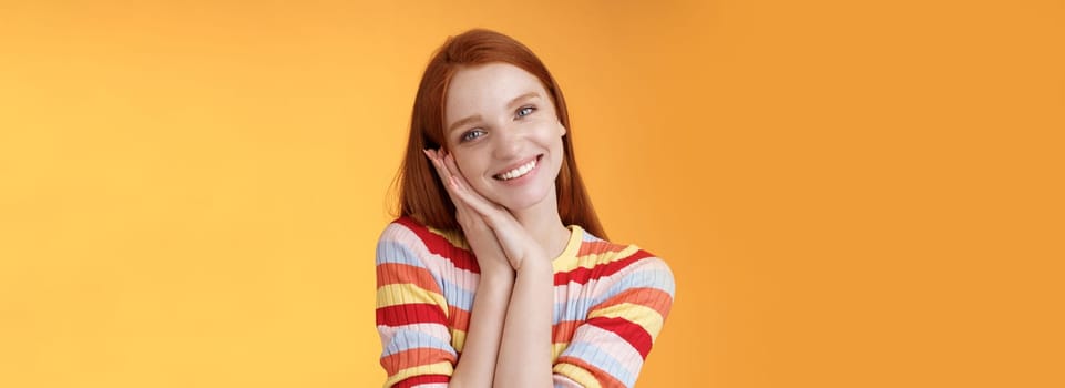 Lovely young flirty redhead european girl smiling broadly excited happy lean palm receive sweet tender present look grateful amused joyfully reacting pleasing moment, standing orange background.