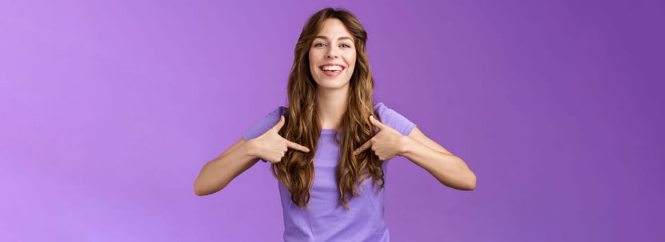 Boastful good-looking curly european female pointing herself proud who she is grinning delighted coming out pride month smiling broadly indicating center chest bragging purple background. Lifestyle.