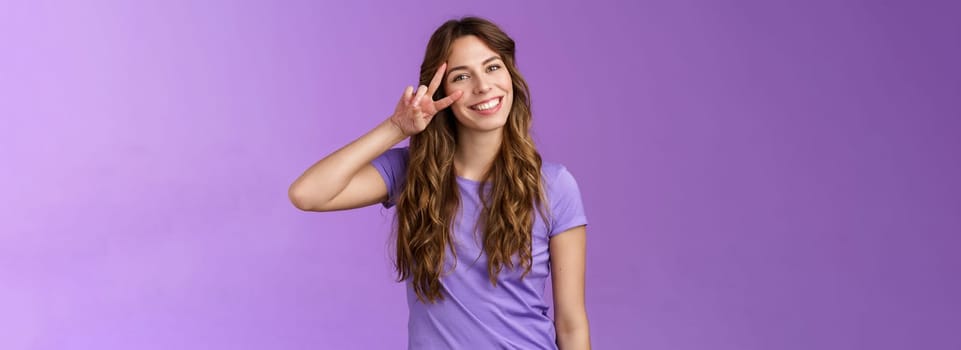 Tender friendly outgoing attractive female tilt head lovely cute gaze show peace victory sign express positivity love cherish friendship stand purple background upbeat relaxed casual pose. Lifestyle.