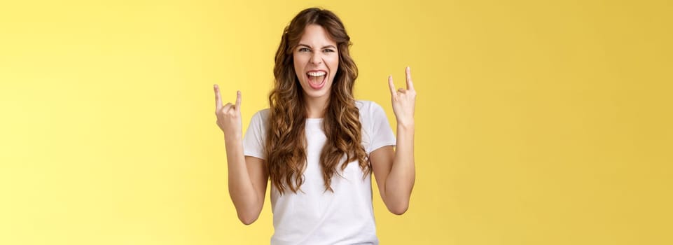 Going wild. Daring amused good-looking european curly-haired girl acting thrilled excited having fun enjoy awesome concert show yeah rock-n-roll heavy metal gesture grimacing satisfied.