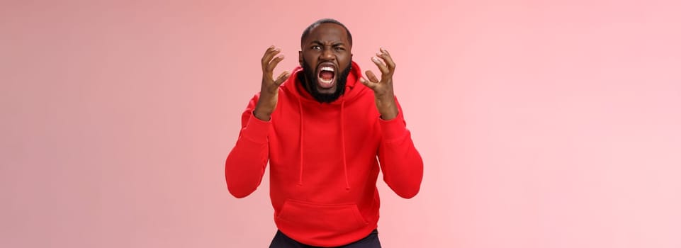 Guy hates subway. Irritated hungry mad bearded african-american man yelling squeez fists frowning grimacing shouting losing temper furiously staring camera go crazy insane, standing pink background.