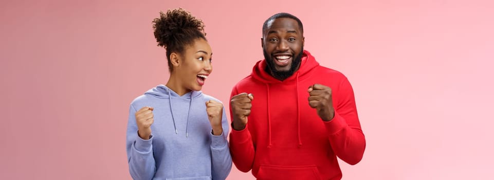 Joyful delighted celebrating african-american woman man standing together happy triumphing clenching fists cheering for favorite team watching match supporting fans celebrating goal win bet.