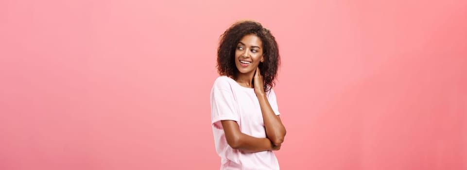 Love in air come and say hi. Flirty sensual good-looking african american young female student with afro hairstyle touching neck gently turning right, gazing with curiousity and desire over pink wall.