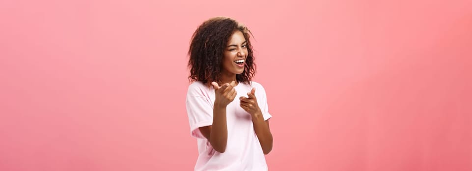 Hey you awesome. Playful charming and happy carefree dark-skinned trendy girl with curly hairstyle winking and smiling broadly making finger gun move towards camera checking out cool outfit.