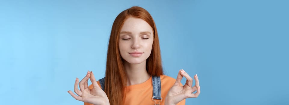 Keep calm redhead relaxed girl stay relieved positive close eyes smiling delighted raising hands sideways lotus mudra gesture practice yoga meditation do breathing exercise, blue background.