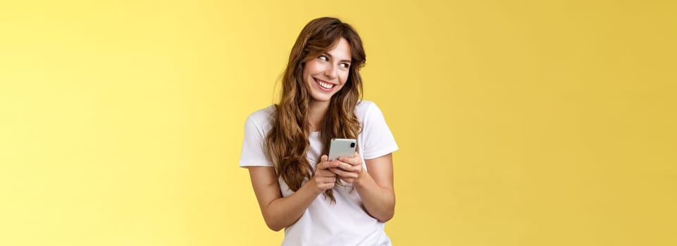 Lovely silly cute flirty girl texting receive romantic lovely gesture look away blushing modest smiling broadly reading bold passionate message stand yellow background joyfully send boyfriend photo. Lifestyle.