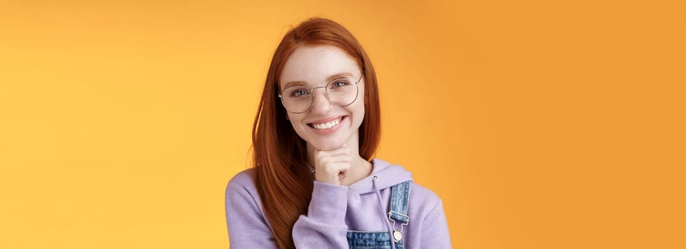 Creative outgoing young charismatic redhead female coworker discuss casual staff smiling laughing happily have pleasant conversation look camera amused tender touch chin, orange background.