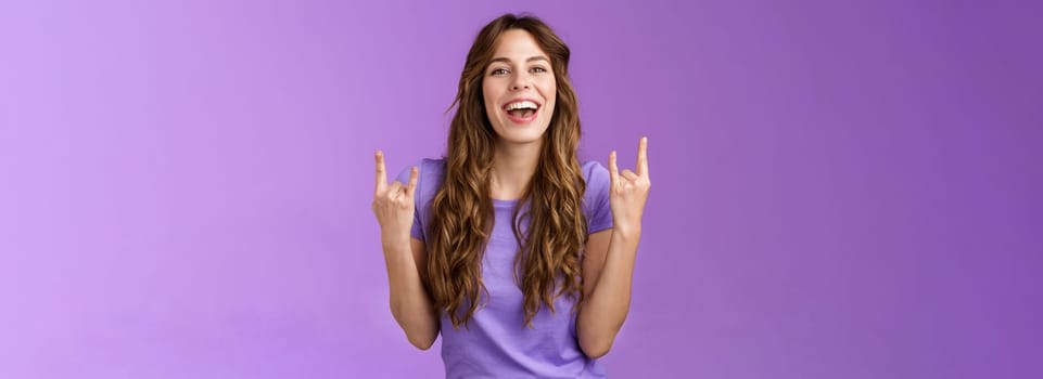 This summer holidays rock. Happy enthusiastic cheerful girl having fun enjoy awesome party weekends smiling broadly say yeah joyful make heavy-metal sign stand purple background amused.