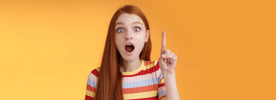 Got idea hurry listen. Excited young emotional redhead female coworker raising index finger eureka gesture open mouth wide eyes shocked thrilled telling excellent plan thinking-up solution.