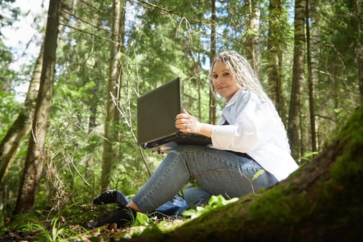 Girl with beautiful dreadlocks and laptop in green forest in spring or summer. Young IT woman, blogger blogging, chatting alone. Need for solitude