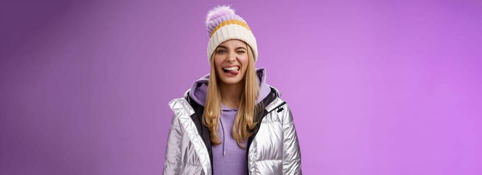 Lifestyle. Cheeky carefree delighted charming blond girl having fun feel amused positive show tongue smiling broadly wearing winter silver glittering jacket stylish hat enjoying awesome ski vacation.