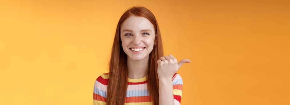Girl pointing left cool person can help smiling delighted look friendly camera discuss interesting project introduce friend during conversation standing happy grinning orange background.