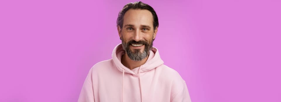 Waist-up happy cheerful caucasian bearded man grey hair in pink trendy hoodie smiling broadly feel healthy attend gym lead active lifestyle grinning white perfect teeth, standing purple background.