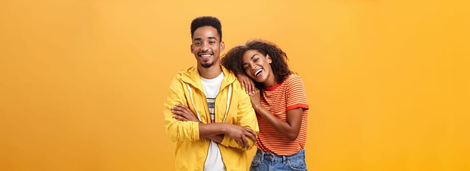 Awesome when boyfriend is best friend. Portrait of charming friendly african american woman leaning on guy touching his shoulder feeling happy they together and she can rely on posing orange wall. Copy space
