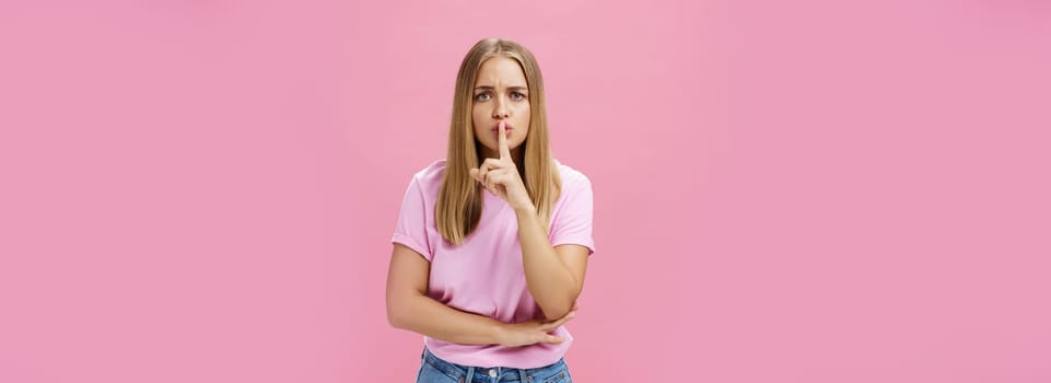 Shh keep voice down. Serious-looking concerned determined female nanny looking after kid asking not speak showing shush gesture with index finger over mouth, having secret concerned someone know it.