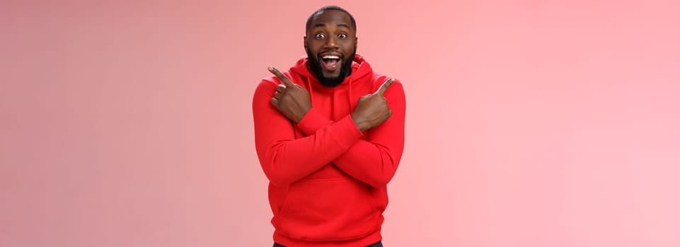 Glad amazed good-looking happy black male customer bearded widen eyes surprised joyfully pointing both sides left right cross arms chest impressed variety cool products, standing pink background.