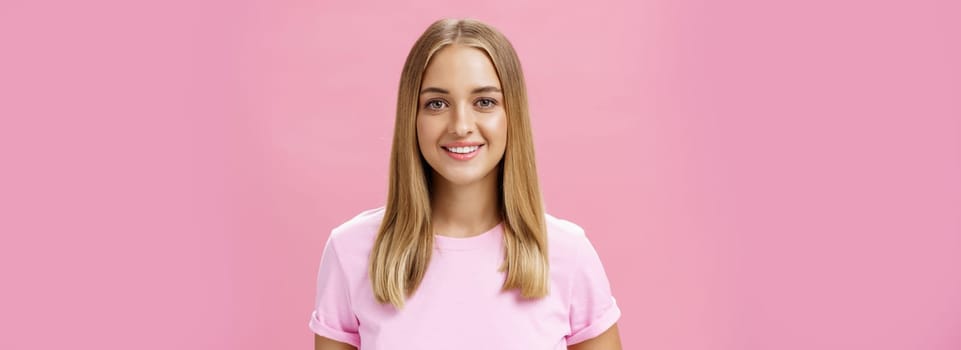 Close-up shot of friendly pleasant commong caucasian girl with fair hair and tanned skin in t-shirt smiling broadly with good white teeth gazing at camera ambitious and delighted over pink background. Lifestyle.