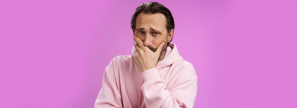 Shocked upset handsome mature bearded man hear terrible news griefing suffer sorrow express empathy gasping hold hand mouth reacting lose cringing crying cannot control emotions, purple background.