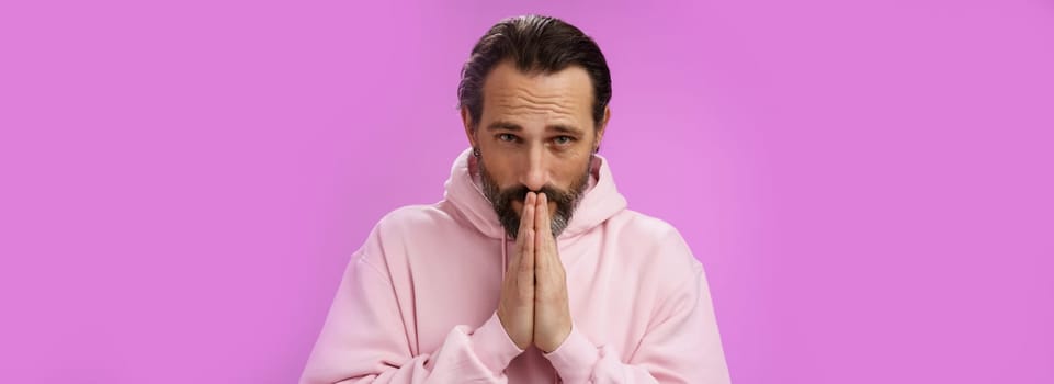 Worried intense serious-looking troubled handsome mature bearded man praying waiting important news nervously looking camera press palms supplicating wish wife alright, standing purple background.
