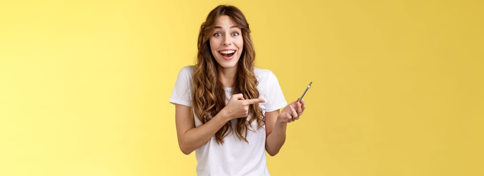Cheerful happy attractive caucasian female curly hairstyle smiling laughing surprised receive pleasant good news via phone call holding smartphone describe awesome post read internet pointing mobile. Lifestyle.