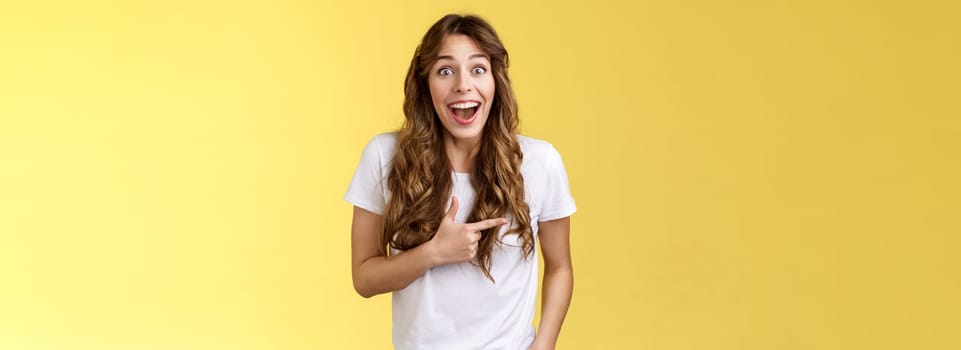 Joyful charismatic woman having fun chatting friend have funny amusing conversation discuss comedy movie pointing left fascinated impressed open mouth smiling broadly laughing yellow background.