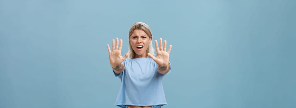 Hold right there. Portrait of intense displeased and irritated attractive young female in blue t-shirt pulling hands towards camera in stop or not gesture frowning and making annoyed expression.