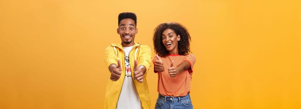 Two friends like perfect and awesome plan. Portrait of joyful friendly-looking optimistic african american female and male showing thumbs up in approval and agreement gesture smiling broadly. Copy space