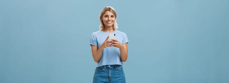 New phone is fantastic. Portrait of satisfied happy young modern blond woman in trendy outfit with blond short haircut smiling joyfull from delight holding smartphone near chest texting or using apps. Technology concept