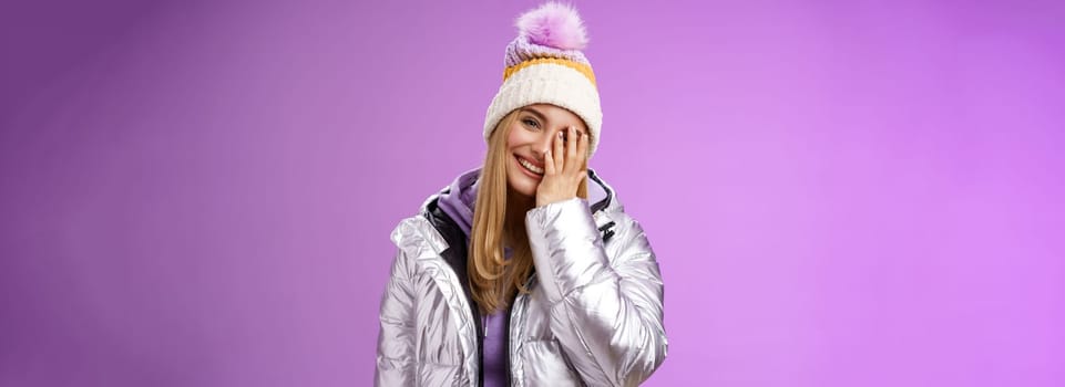 Carefree happy upbeat charming blond woman cover half face tilting head laughing joyfully wearing outdoor stylish silver jacket winter hat having fun awesome five star ski resort, purple background.
