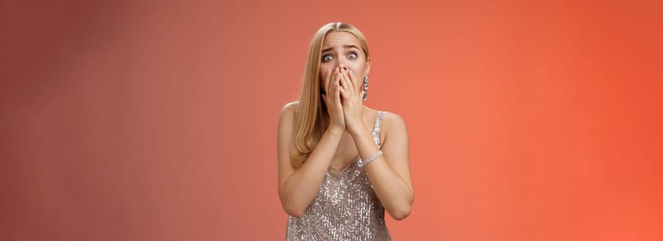 Shocked afraid insecure terrified unconfident concerned young blond woman in silver stylish dress gasping horrified pop eyes stunned red background look afraid, panicking witness crime.