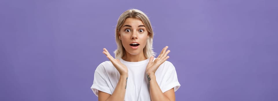 Lifestyle. Close-up shot of charmed and impressed good-looking caucasian girlfriend with blond hair and tattoos on arms raising hands in amazed and excited gesture opening mouth and gazing mesmerized at camera.