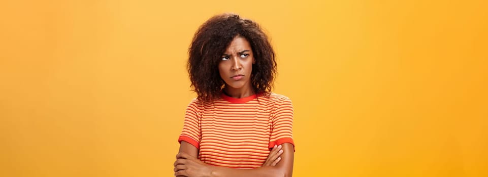 Why life so cruel and unfair. Gloomy displeased and sad cute african american young woman with curly hairstyle crossing arms on chest in offended pose frowning looking left jealous and unhappy.